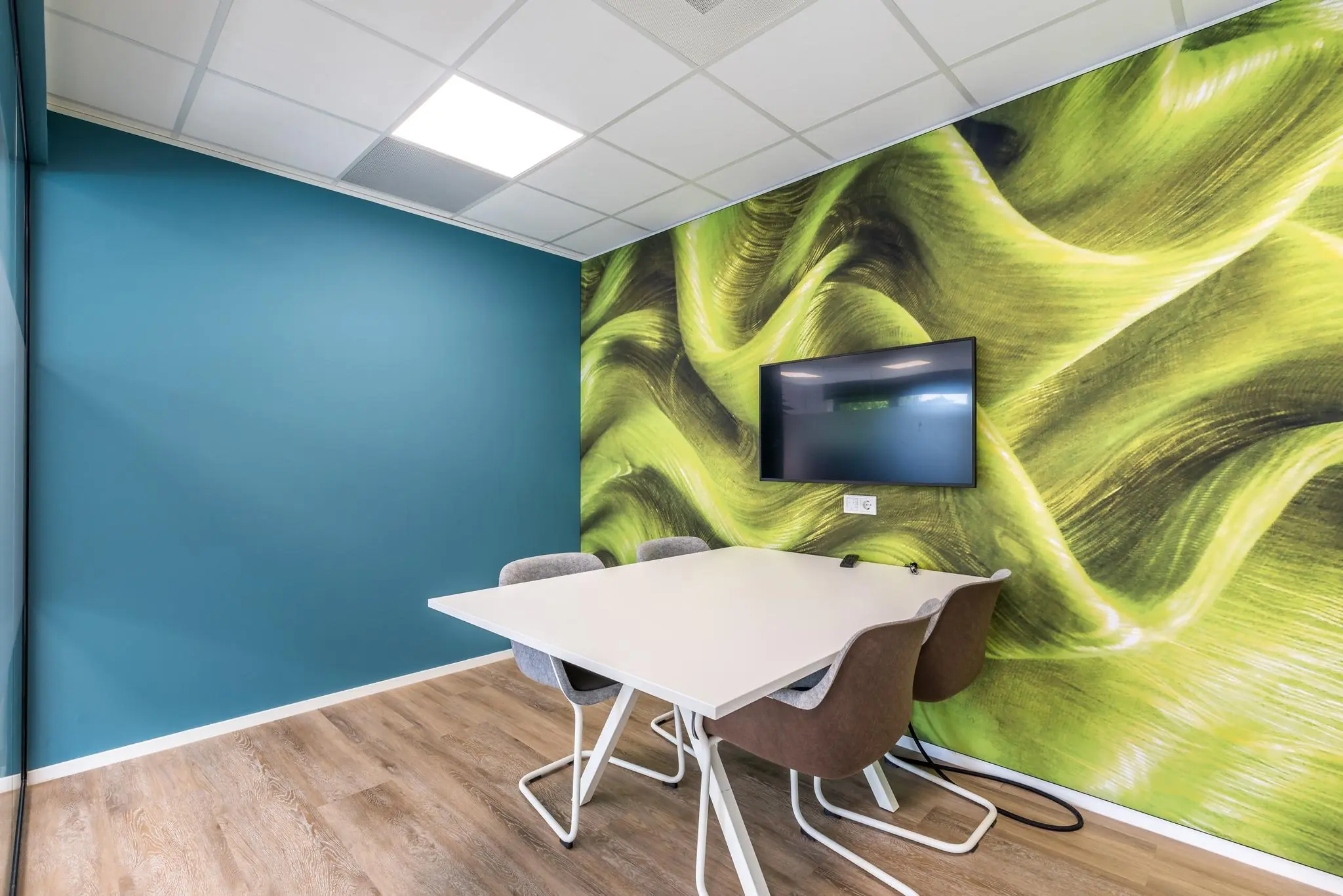 Moderne vergaderruimte aan de Baarnsche Dijk met kleurrijke muur, flatscreen en vier stoelen rondom een witte tafel.